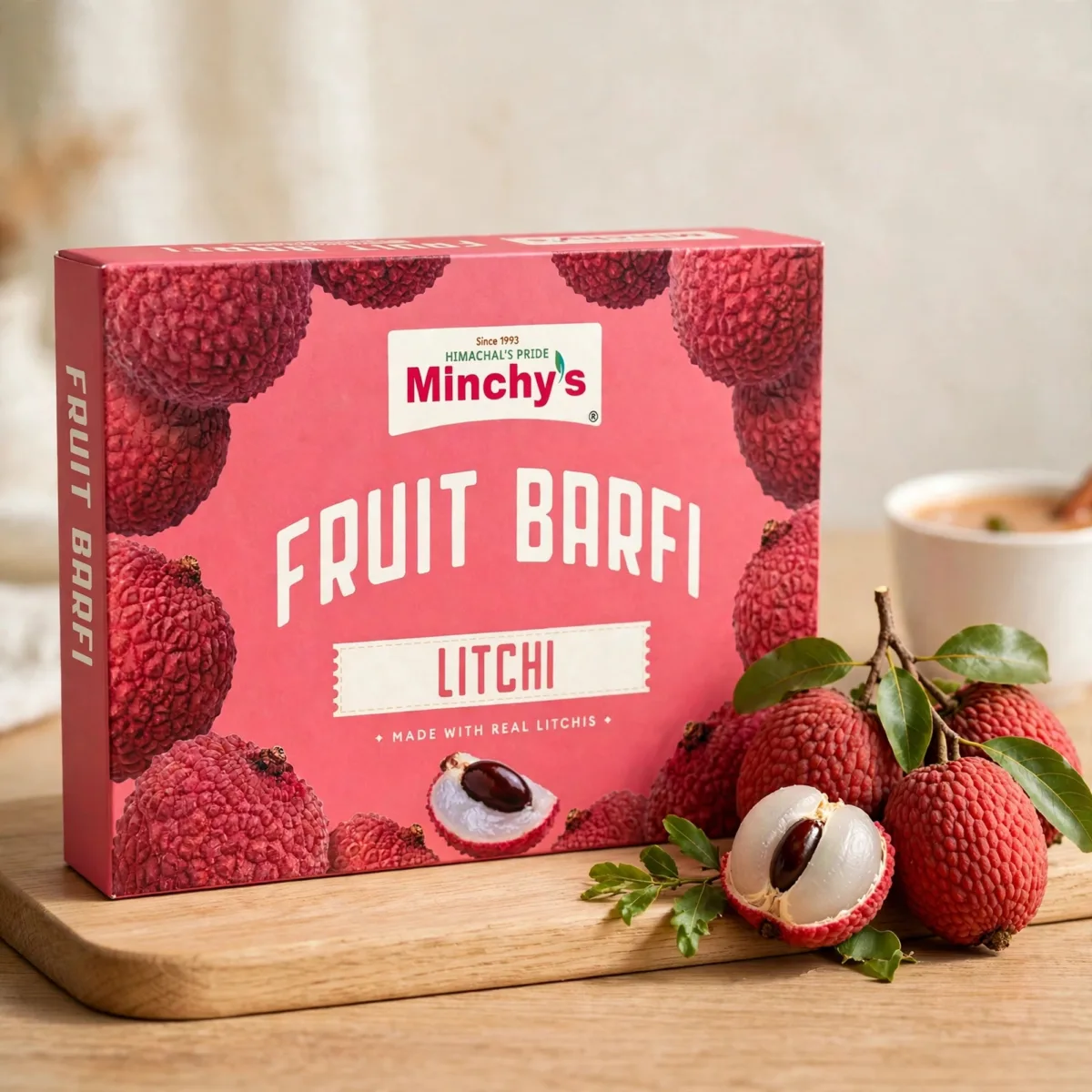 Minchy's Litchi Fruit Barfi 250 g box with fresh litchi fruit on a wooden board