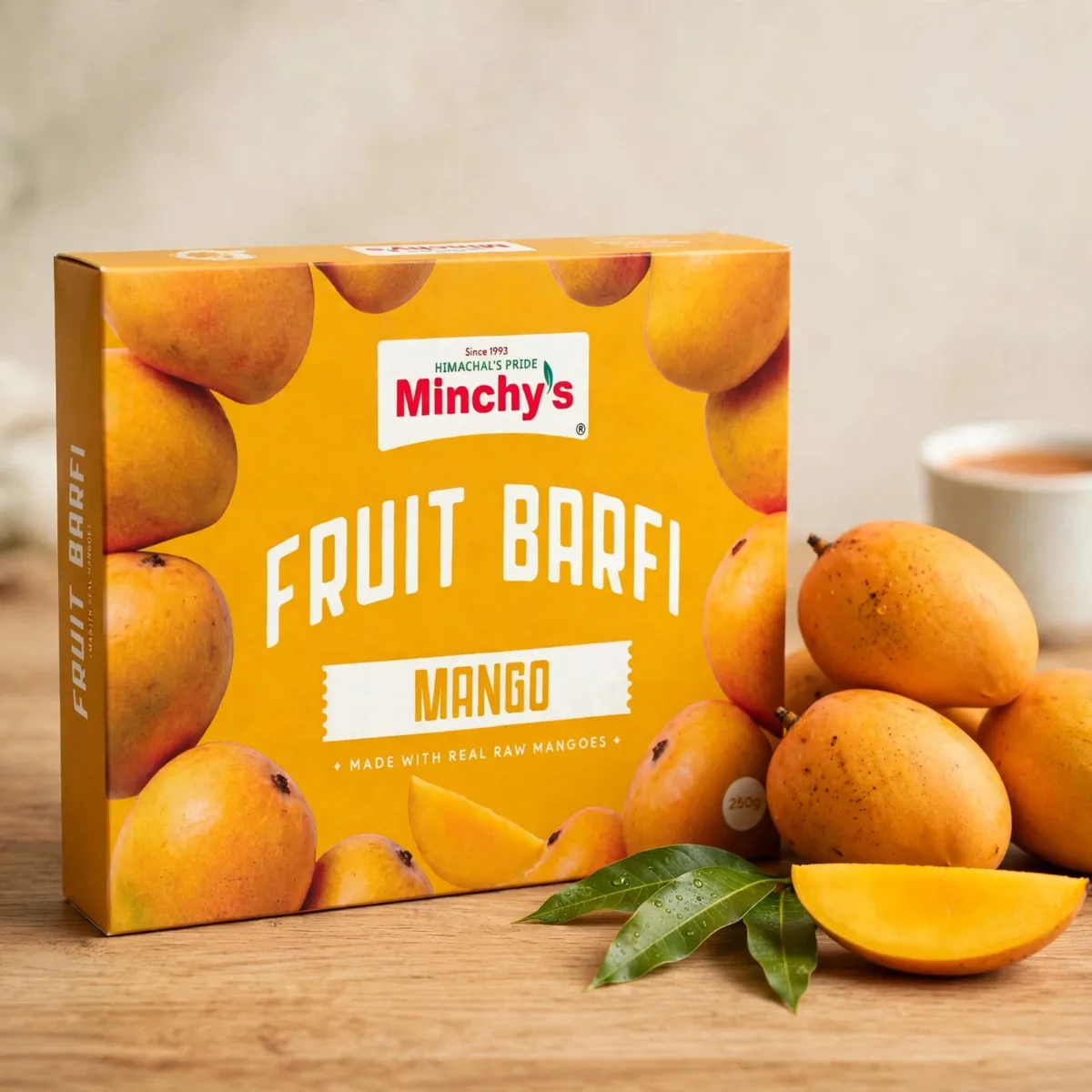 Minchy's Mango Fruit Barfi 250 g box with fresh mango fruit on a wooden board